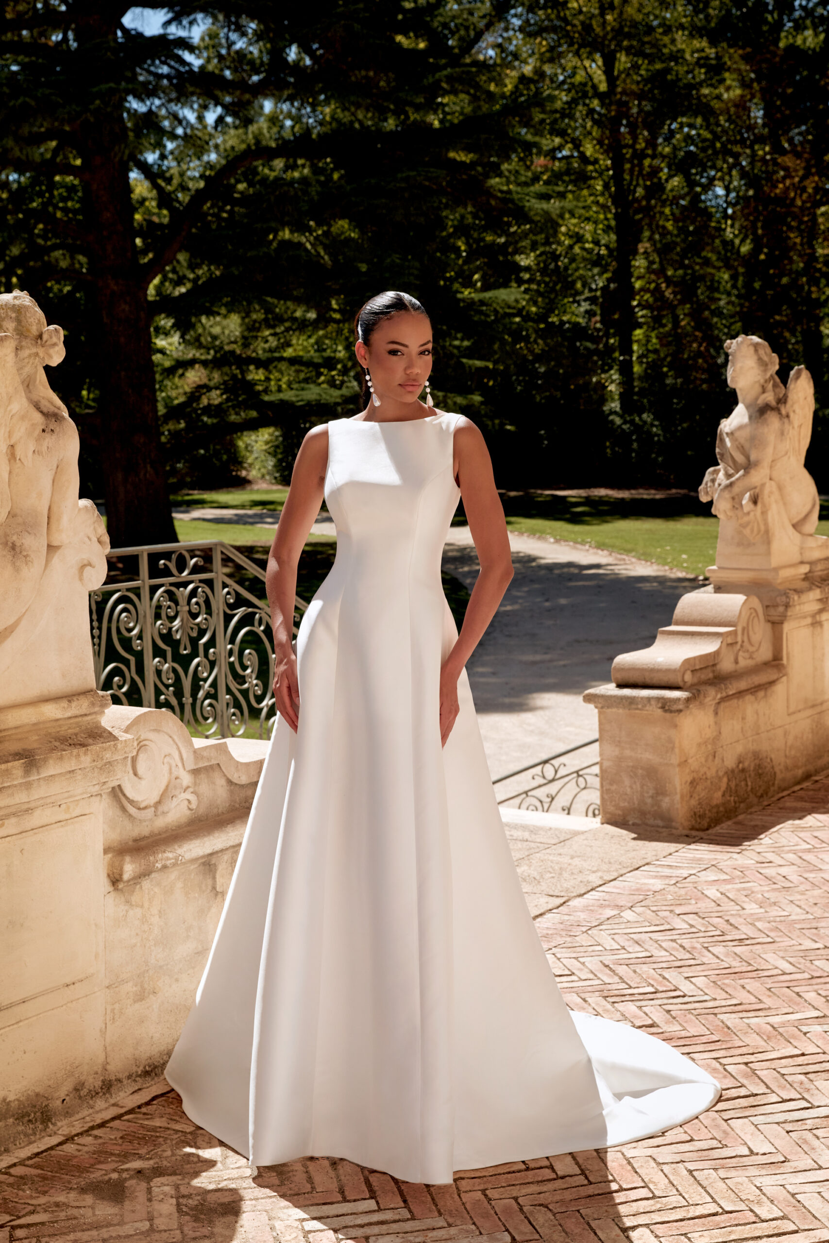 Das Brautkleid ist aus Satin und hat einen U-Boot Ausschnitt. Der tiefe Rückenausschnitt wird mit einer Schleife und einer Knopfleiste abgerundet.