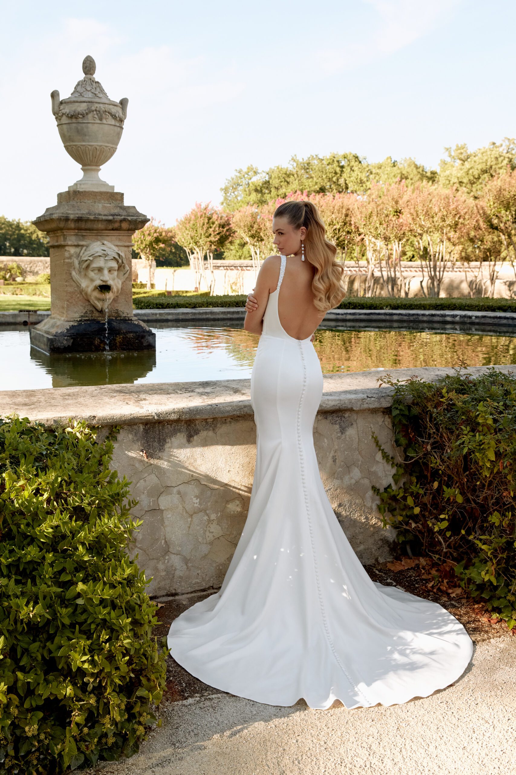 Brautkleid aus Satin mit Drapierungen im Vorderteil, Tiefer Rückenausschnitt und Perlendetails am Träger und Ausschnitt. Das Kleid wird abgerundet von einer Knopflochleiste in der Rückenmitte und einer schönen Schleppe