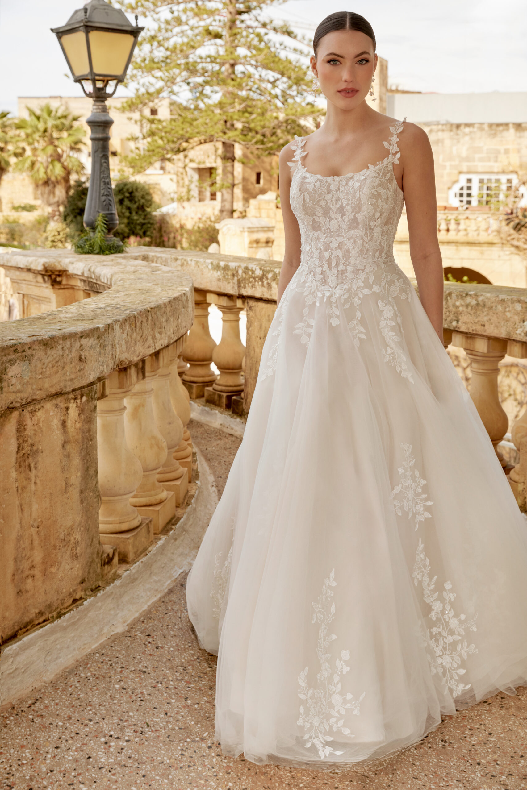 Das Brautkleid ist aus Tüll und mit Blumenapplikationen verziert. Die Spaghettiträger haben die selbe Spitze. Der Ausschnitt vorne ist rund und hinten tiefer.